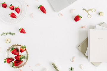 Frame of feminine modern home office desk with laptop, notebook, lipstick, fresh raw strawberries and rose flower buds on white background. Flat lay, top view.