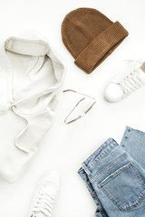 Woman casual fashion clothes and accessory set on white background. Hoody, boyfriend jeans, hat, sneakers, sunglasses. Flat lay, top view.