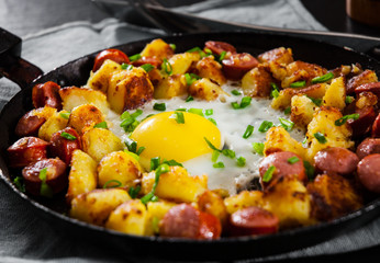 fried egg with sausage and potato in a frying pan on wooden table
