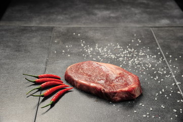 Raw steak with hot pepper on a granite table.