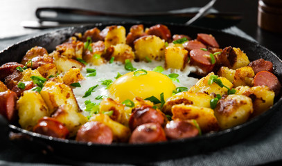 fried egg with sausage and potato in a frying pan on wooden table