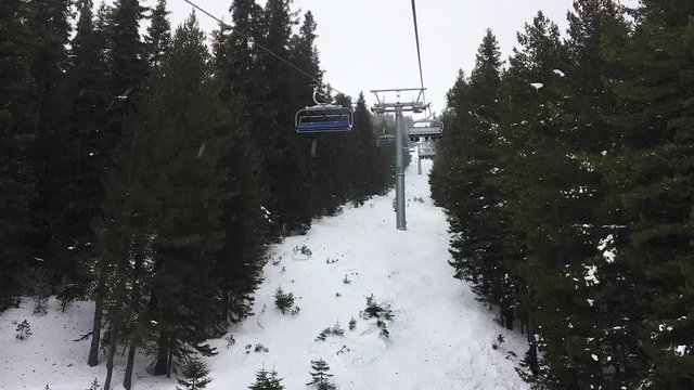 1080 HD time lapse hyper lapse video clip of four person ski chair lift climbing through forest trees on a misty mountain