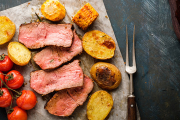 Sliced Roast beef on cutting board with grilled vegetables. View from above