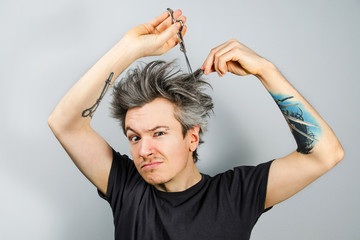 Unshorn and unshaven young guy with piercings on his face, shears her hair and looks in camera, on...