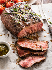 Sliced Roast beef on white paper on wooden table with grilled vegetables.