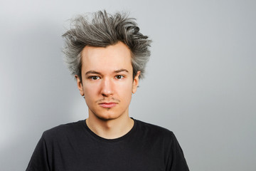 Unshorn and unshaven young guy looks in camera, on gray background.