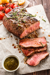 Sliced Roast beef on white paper on wooden table with grilled vegetables.