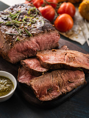 Sliced Roast beef on cutting board with grilled vegetables .