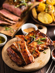 Delicious barbecued ribs seasoned with a spicy basting sauce and served with chopped fresh vegetables on an old rustic wooden chopping board