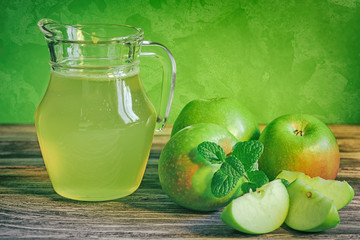 A decanter of apple juice with green apples on a wooden table, close-up