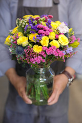 Beautiful bouquet in yellow, pink, blue colors of roses, statice and other flowers in the male florist hands.
