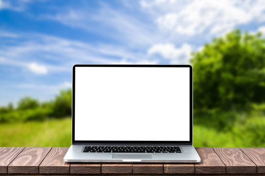 Modern laptop with empty white screen on wooden table against blurred landscape