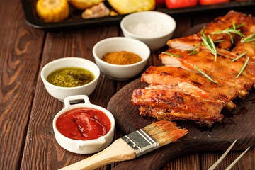 Delicious barbecued ribs seasoned with a spicy basting sauce and served with chopped fresh vegetables on an old rustic wooden chopping board