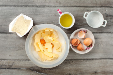 Table top  view on ingredients for cake preparation. Sack of flour, bowl with butter and eggs yolk, cup with glair, egg shells and sugar, placed on gray wood desk.