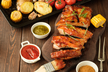 Delicious barbecued ribs seasoned with a spicy basting sauce and served with chopped fresh vegetables on an old rustic wooden chopping board