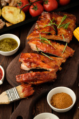 Delicious barbecued ribs seasoned with a spicy basting sauce and served with chopped fresh vegetables on an old rustic wooden chopping board