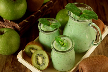 Green smoothie made of kiwi, apple and mint in glass jars surrounded by fruits
