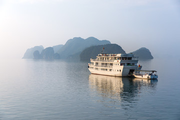 Big tourist cruise boat on the quiet water of Halong Bay (Unesco Heritage site) during late afternoon on the backdrop of a limestone rock mountain. Halong Bay, Vietnam.