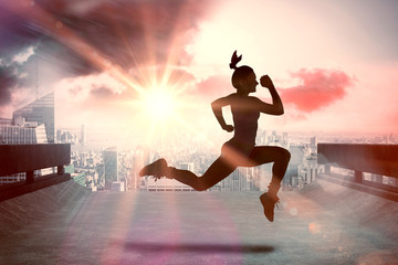 Fit brunette running and jumping against sun shining over road and city