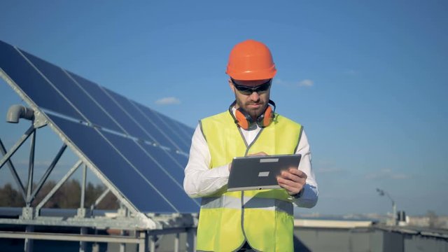 A worker uses tablet, counting solar panels on a roof. 4K.