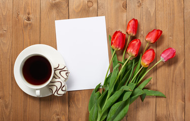 tulips are on wooden boards, cup of coffee, blank paper sheet with place for text - holiday and greeting concept