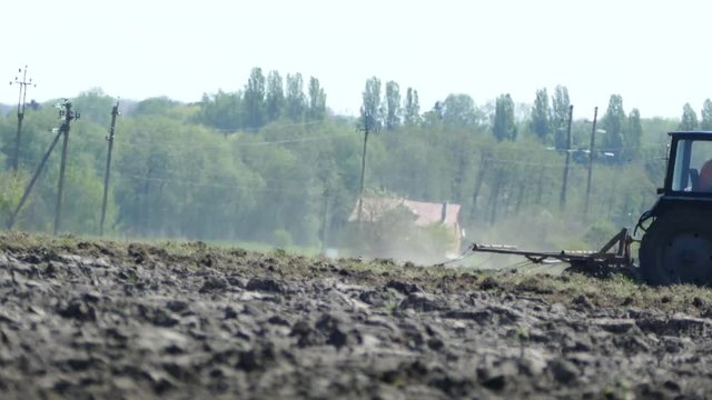 A tractor sowing seed in the field in the spring. The farmer works in his field. Dust rises behind the passing tractor.