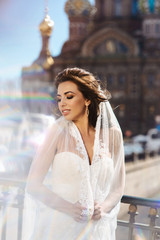 Naklejka premium Close up portrait of beautiful young caucasian brunette woman bride in white wedding dress over Saint-Petersburg on blurred background. Smiling girl in wedding dress