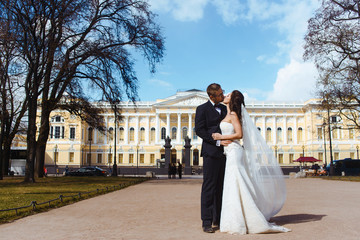 Obraz premium Newlywed couple bride and groom photoshoot after wedding ceremony in Saint-Petersburg Russia. White wedding dress with long veil and classical black suit or smoking with bowtie. Businessman in glasses