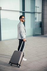 Businessman walking from hotel lobby. Full length portrait of young executive with a suitcase.