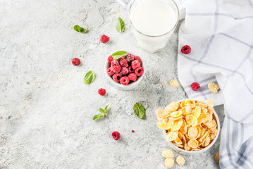 Healthy breakfast ingredients. Breakfast cereal flakes, milk or yogurt glass, raspberries and mint on grey stone background, copy space