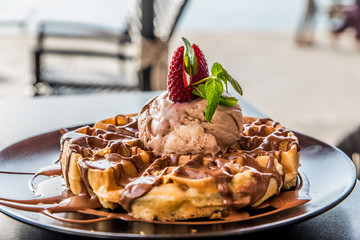 A Belgian waffle with a ball of chocolate syrup of chocolate and a strawberry on the top