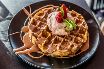 A Belgian waffle with a ball of chocolate syrup of chocolate and a strawberry on the top