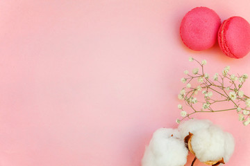 Top view of mini pink macaron or macaroon french desserts cake with cotton flowers on soft sweet pink pastel geometric paper flat lay background.