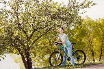 Naklejka premium Young woman with bicycle on nature. Blossoming tree in spring