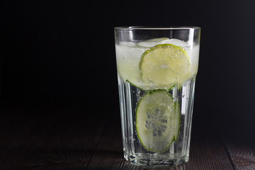 Cold drink with ice, cucumber and lime on dark low key background