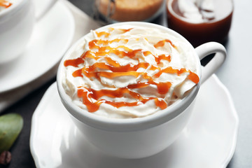Cup of coffee with caramel topping on table, closeup