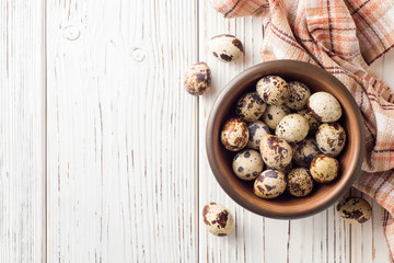 Fresh quail eggs in ceramic bowl on white wooden background