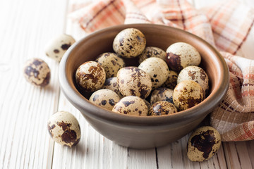 Fresh quail eggs in ceramic bowl on white wooden background