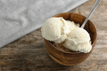 Wooden bowl with tasty vanilla ice cream on table