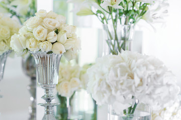Decoration of a festive banquet with white vibrant flowers in glass vases on a white background