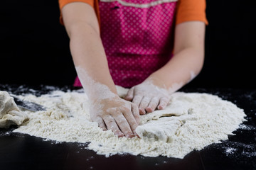 Obraz na płótnie Canvas Kneading dough on a black table in a bakery. Baker's hands preparing dough for bread.