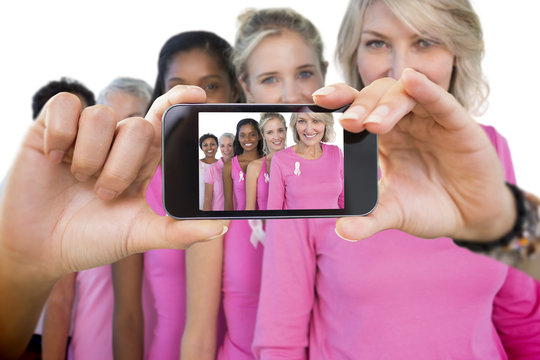 Composite image of hand holding smartphone showing photograph of breast cancer activists