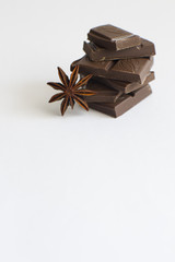 pyramid of chocolate pieces and star anise on white background with empty space, vertically