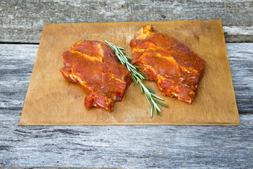 Two raw steaks with spices on wooden rustic board on dark wooden table. Ready for cooking.