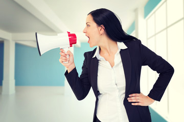 Pretty businesswoman shouting with megaphone against modern blue and white room