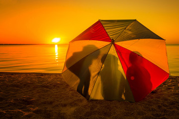 three children at sunset near a lake in the sand under a beach umbrella