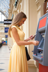 Fototapeta na wymiar Happy blonde woman withdrawing money from credit card at ATM
