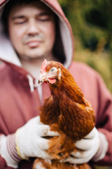 Farmer with red chicken on his hands isolated on nature green background