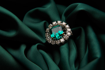 Green emerald fashion engagement diamond ring on green satin background. Luxury female jewellery,...