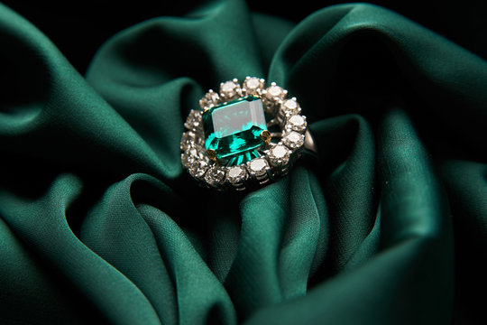 Green emerald fashion engagement diamond ring on green satin background. Luxury female jewellery, close-up. Selective focus